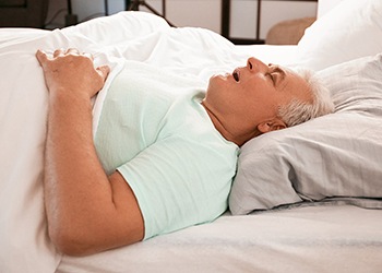 An older gentleman lying asleep in bed with his mouth open and snoring