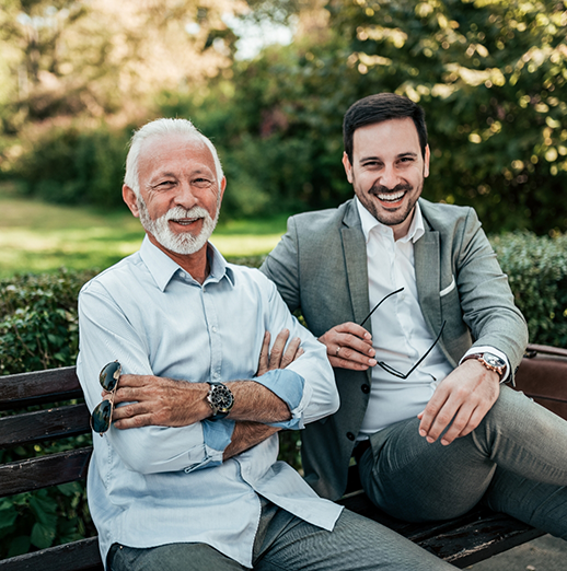 Two men sitting on a park bench and smiling after seeing a dentist near Lewis Center