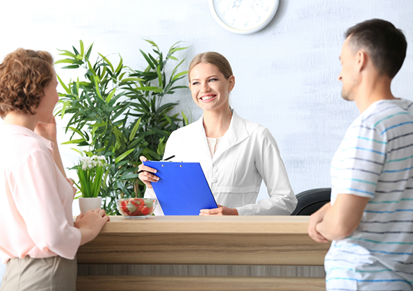 Dental office receptionist smiling at two patients