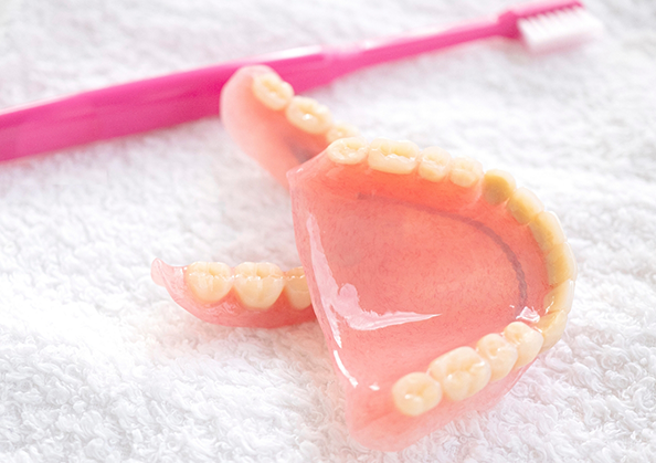 Two dentures resting on a towel next to a toothbrush