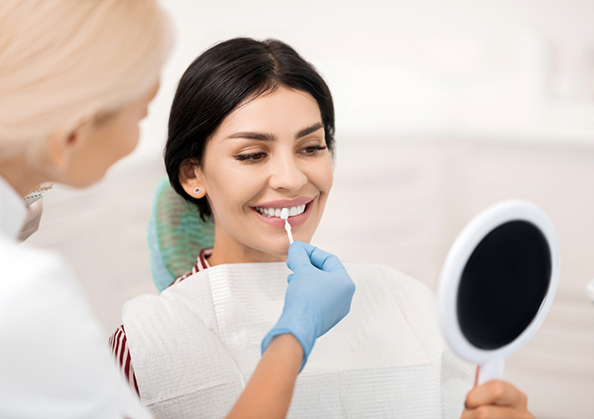 Dentist holding a veneer in front of a patient's smile