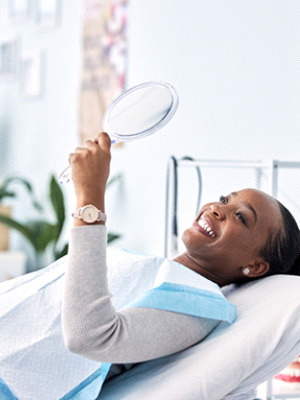 Woman smiling at reflection in handheld mirror