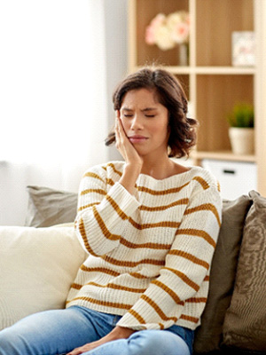 Woman experiencing toothache sitting on couch at home