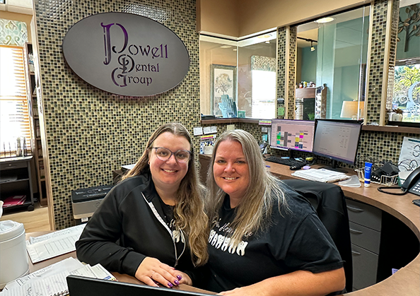 Two Powell Dental Group team members smiling behind a desk