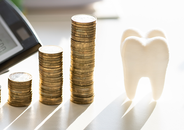 Three stacks of coins next to a model of a tooth